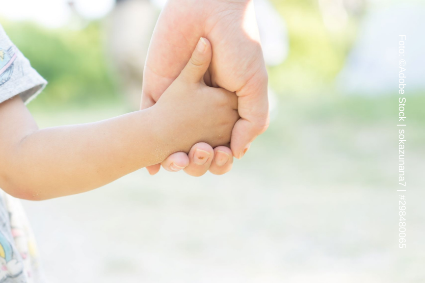 Eine Kinderhand hält die Hand einer erwachsenen Person.